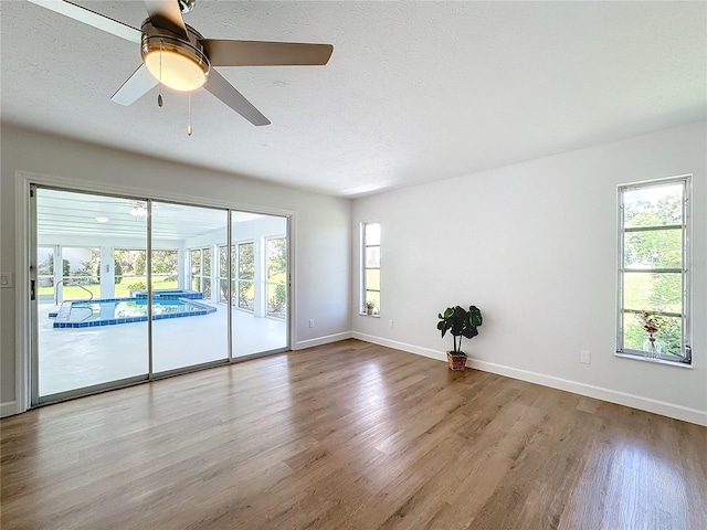 empty room featuring a wealth of natural light, light hardwood / wood-style flooring, a textured ceiling, and ceiling fan