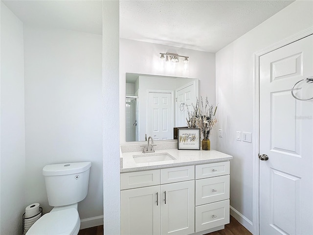 bathroom with a textured ceiling, walk in shower, wood-type flooring, toilet, and vanity