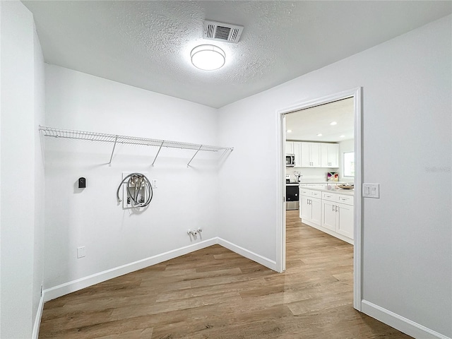 clothes washing area featuring light hardwood / wood-style floors, a textured ceiling, and hookup for a gas dryer