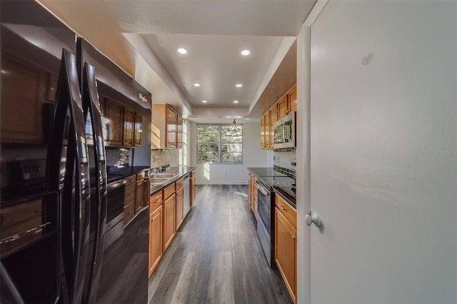 kitchen with dark wood-type flooring, stainless steel appliances, a tray ceiling, sink, and tasteful backsplash