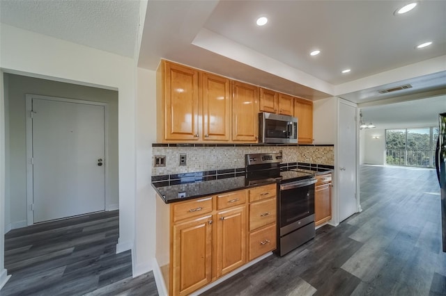 kitchen with dark stone countertops, backsplash, stainless steel appliances, and dark hardwood / wood-style flooring