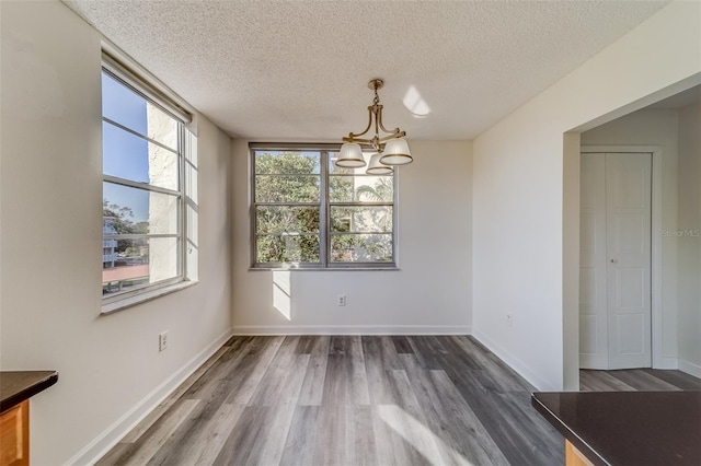 unfurnished dining area featuring a notable chandelier, a textured ceiling, and dark hardwood / wood-style flooring