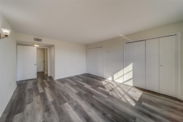 unfurnished bedroom featuring a textured ceiling, multiple closets, and dark hardwood / wood-style flooring