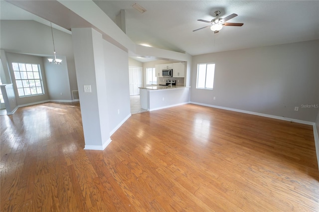 unfurnished living room with a wealth of natural light, light hardwood / wood-style flooring, ceiling fan with notable chandelier, and vaulted ceiling