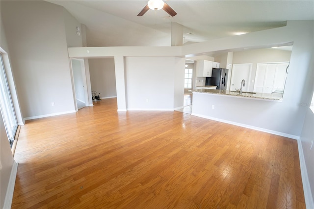 unfurnished living room featuring light wood-type flooring, vaulted ceiling, ceiling fan, and sink