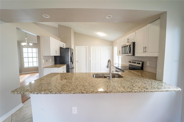 kitchen with sink, kitchen peninsula, lofted ceiling, white cabinets, and appliances with stainless steel finishes