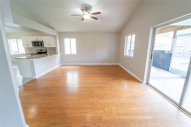 unfurnished living room featuring ceiling fan, light hardwood / wood-style flooring, a healthy amount of sunlight, and vaulted ceiling