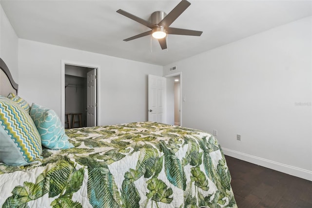 bedroom with dark wood-type flooring, a walk in closet, a closet, and ceiling fan