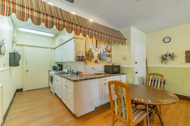 kitchen with white cabinets, tasteful backsplash, a textured ceiling, light wood-type flooring, and white stove