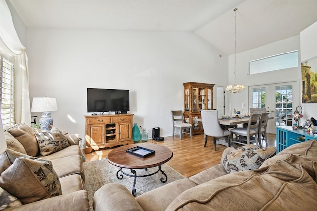 living room with a chandelier, french doors, high vaulted ceiling, and light wood-type flooring