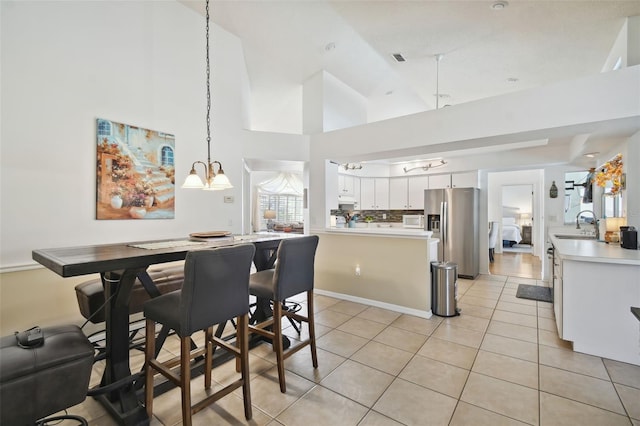 tiled dining room with sink, a notable chandelier, and high vaulted ceiling