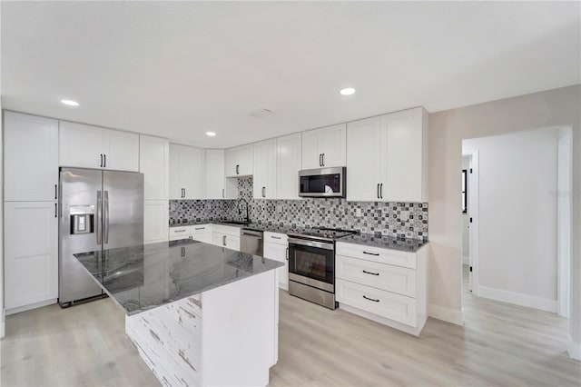 kitchen with sink, appliances with stainless steel finishes, dark stone counters, a center island, and light wood-type flooring