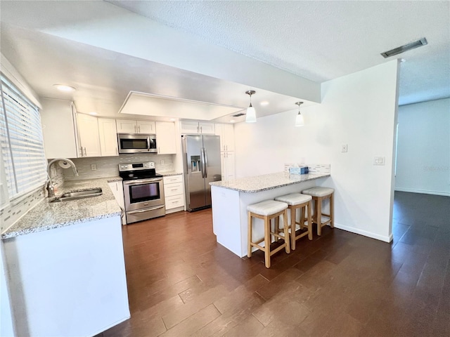 kitchen featuring dark hardwood / wood-style floors, hanging light fixtures, stainless steel appliances, sink, and white cabinets