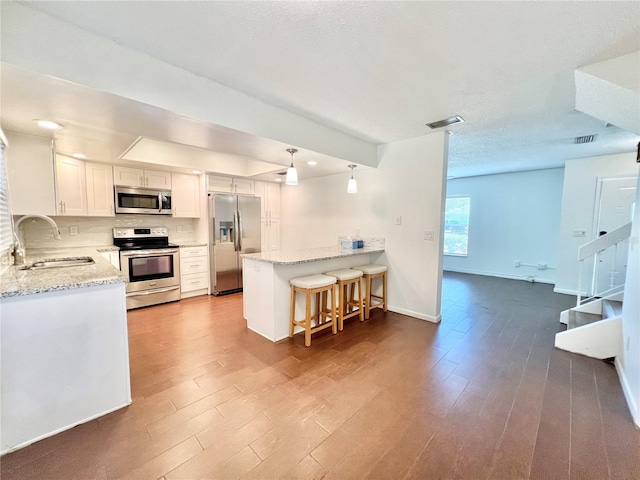 kitchen with sink, kitchen peninsula, white cabinetry, stainless steel appliances, and hardwood / wood-style flooring