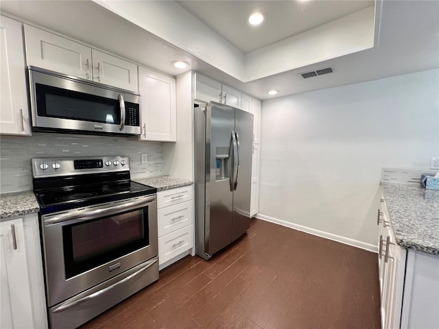 kitchen with decorative backsplash, white cabinets, dark hardwood / wood-style flooring, light stone countertops, and stainless steel appliances