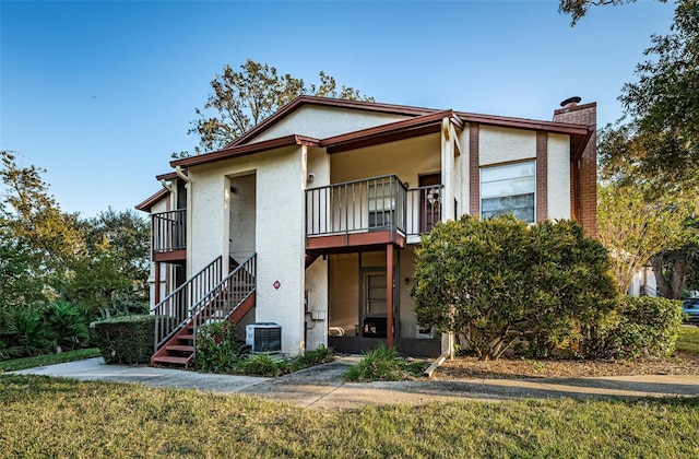 view of front of home with a front lawn, central AC unit, and a balcony