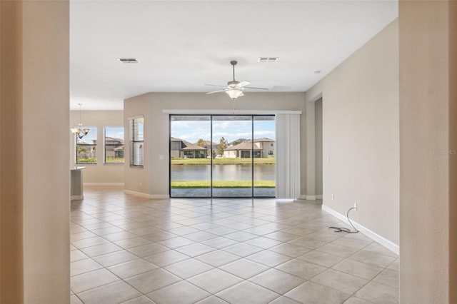 spare room featuring a water view, light tile patterned floors, and ceiling fan with notable chandelier