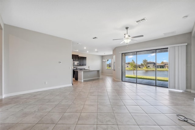 unfurnished living room with a water view, ceiling fan, light tile patterned flooring, and sink