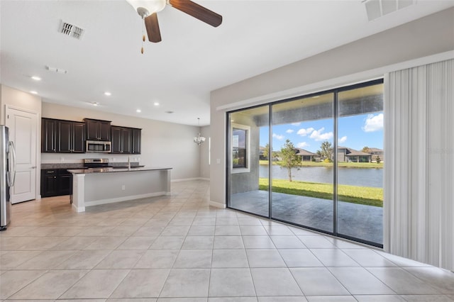 kitchen featuring light tile patterned floors, a kitchen island with sink, sink, stainless steel appliances, and a water view