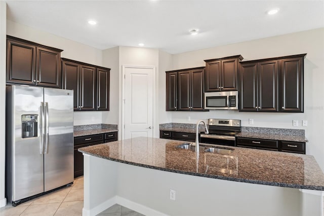 kitchen featuring sink, an island with sink, stainless steel appliances, dark stone countertops, and light tile patterned floors