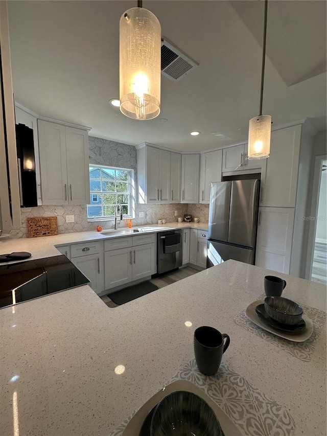 kitchen with stainless steel appliances, sink, decorative light fixtures, white cabinetry, and light stone counters