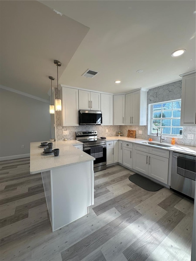 kitchen with kitchen peninsula, white cabinets, appliances with stainless steel finishes, decorative light fixtures, and sink