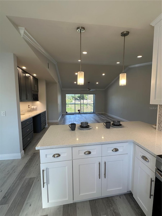 kitchen featuring light stone countertops, white cabinets, kitchen peninsula, and pendant lighting