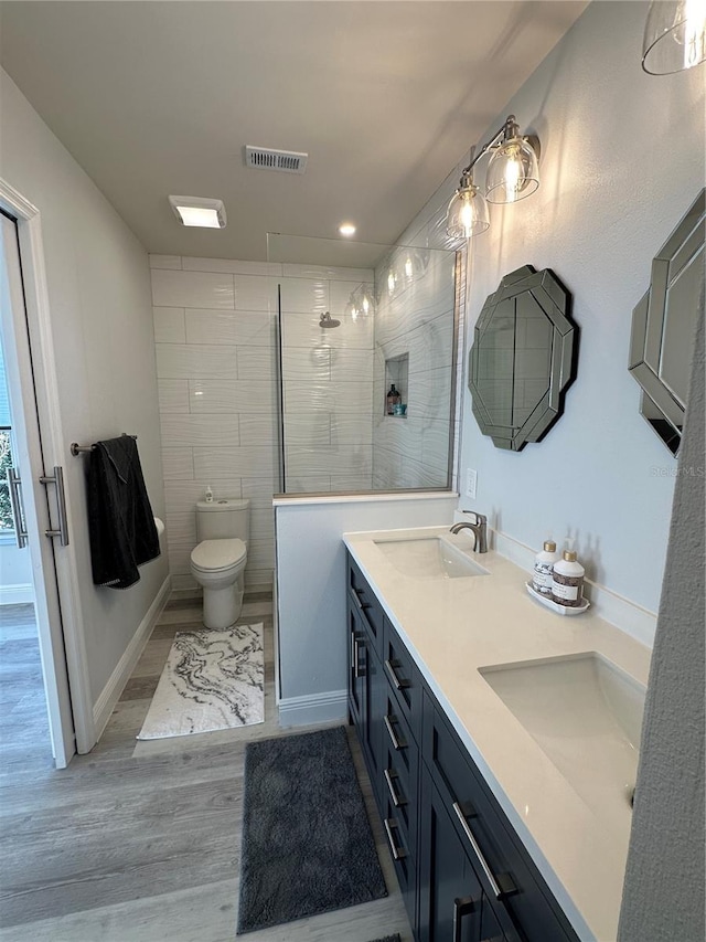 bathroom featuring hardwood / wood-style floors, a tile shower, tile walls, toilet, and vanity