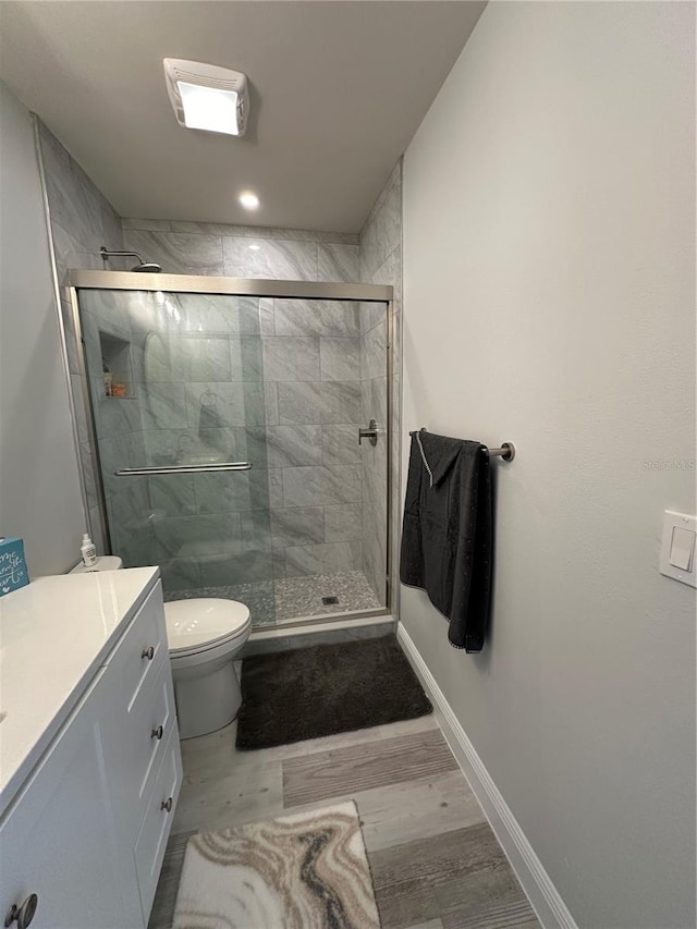 bathroom featuring vanity, toilet, wood-type flooring, and a shower with door