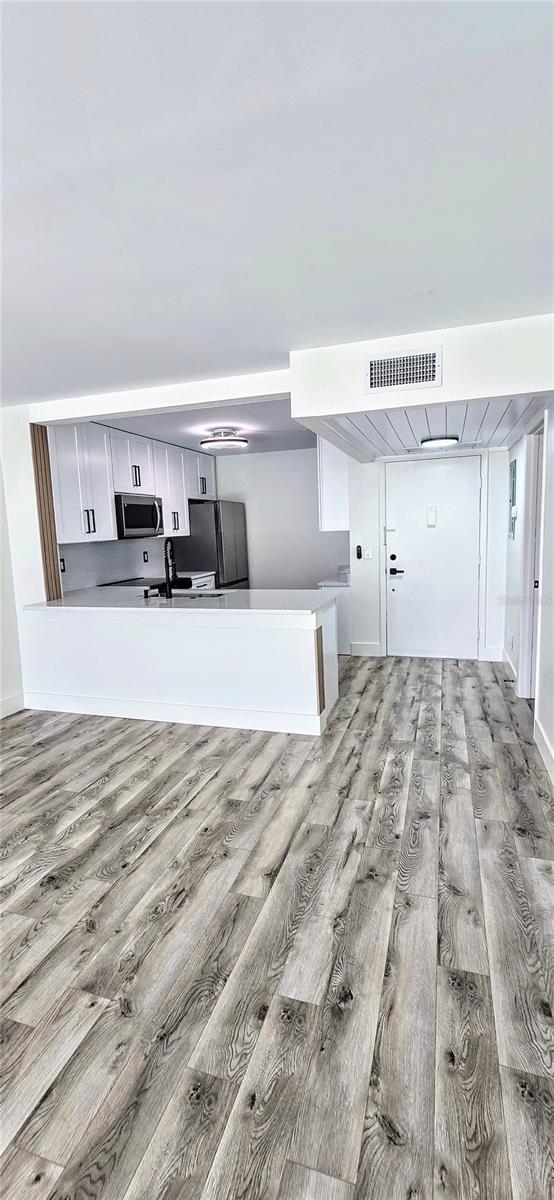 kitchen with appliances with stainless steel finishes, kitchen peninsula, white cabinets, and light hardwood / wood-style floors