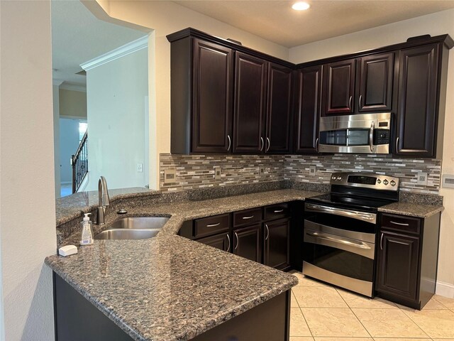 kitchen with appliances with stainless steel finishes, tasteful backsplash, sink, dark stone counters, and dark brown cabinets