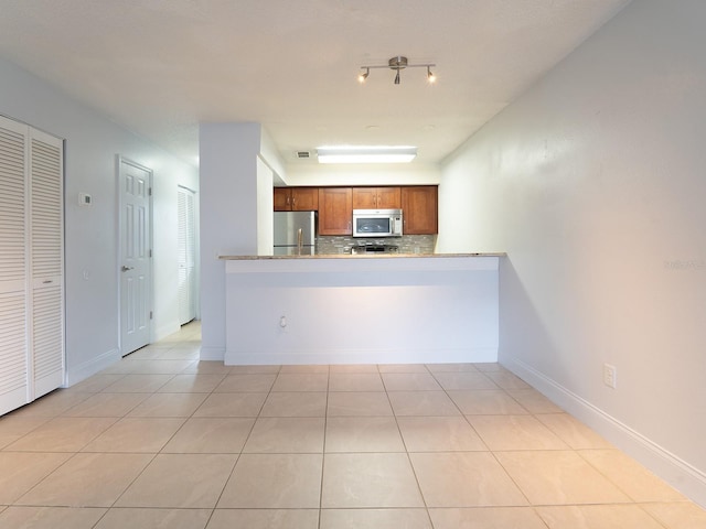 kitchen with kitchen peninsula, light tile patterned flooring, stainless steel fridge, and decorative backsplash