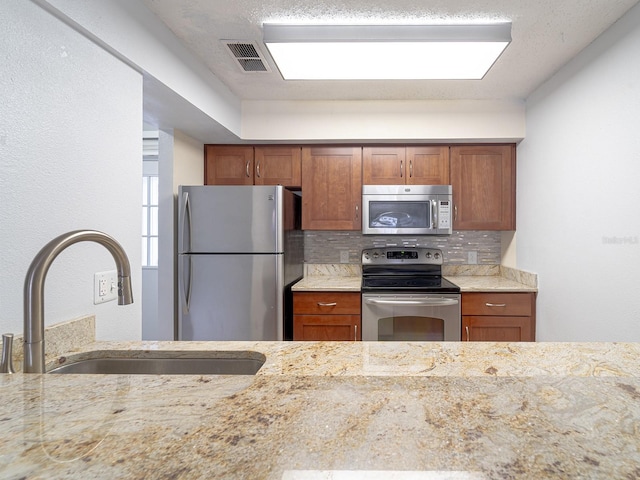 kitchen with sink, decorative backsplash, light stone counters, and appliances with stainless steel finishes