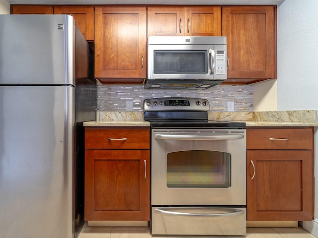 kitchen with light stone countertops, appliances with stainless steel finishes, light tile patterned floors, and decorative backsplash