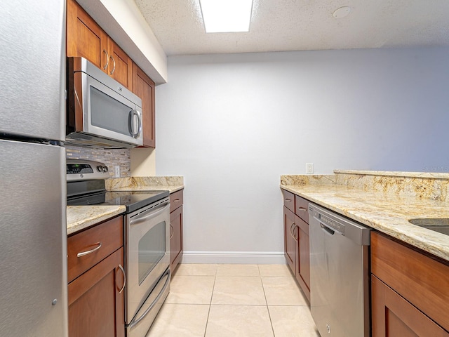 kitchen featuring stainless steel appliances, light stone countertops, light tile patterned floors, a textured ceiling, and tasteful backsplash