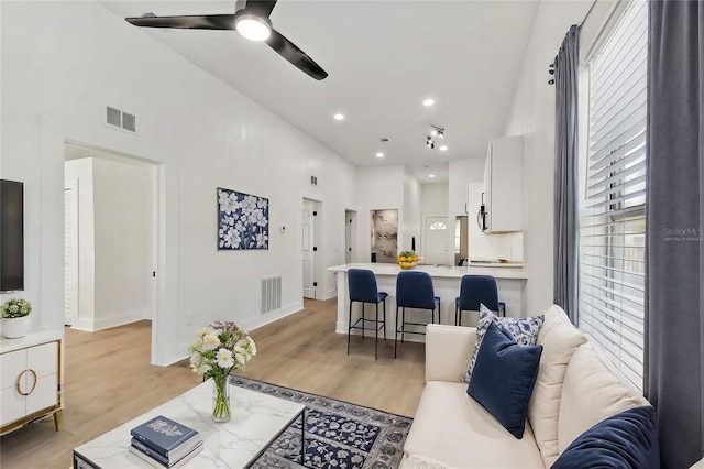 living room with a towering ceiling, light hardwood / wood-style flooring, and ceiling fan