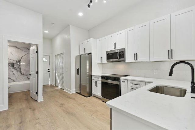 kitchen with stainless steel appliances, sink, light stone countertops, light wood-type flooring, and white cabinetry