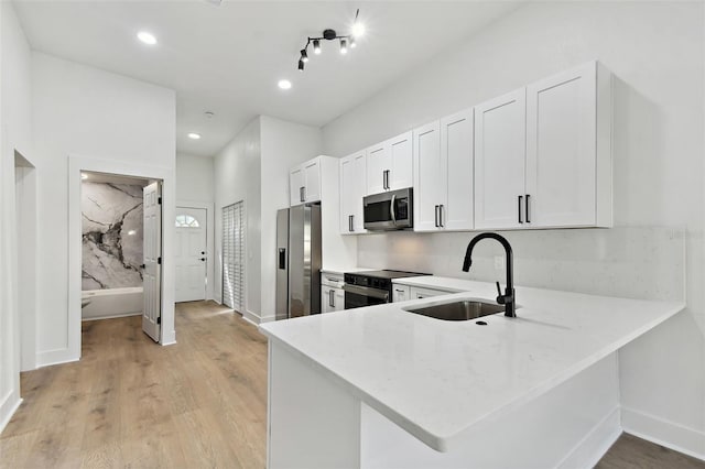 kitchen featuring kitchen peninsula, sink, white cabinets, appliances with stainless steel finishes, and light hardwood / wood-style floors