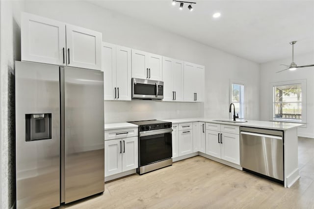 kitchen with sink, kitchen peninsula, stainless steel appliances, white cabinets, and light hardwood / wood-style flooring