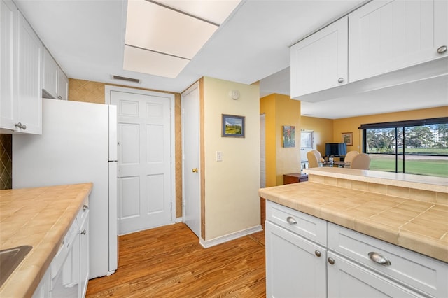 kitchen with tile countertops, white cabinetry, white fridge, decorative backsplash, and light hardwood / wood-style flooring