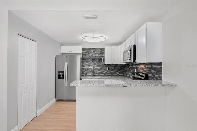 kitchen with kitchen peninsula, light stone counters, white cabinetry, light wood-type flooring, and stainless steel appliances