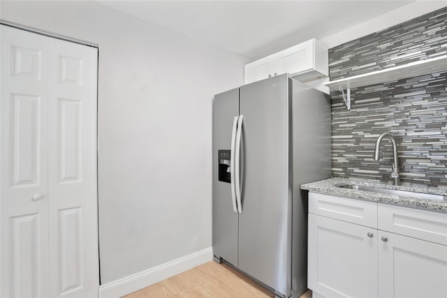 kitchen featuring decorative backsplash, sink, light stone countertops, stainless steel fridge with ice dispenser, and white cabinetry