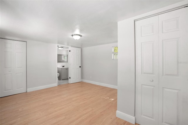 unfurnished bedroom featuring two closets, light wood-type flooring, and ensuite bath