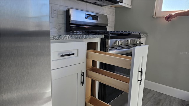 kitchen with stainless steel gas range oven, white cabinetry, hardwood / wood-style flooring, dark stone counters, and refrigerator