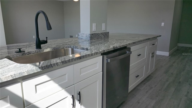 kitchen with wood-type flooring, sink, stainless steel dishwasher, white cabinetry, and light stone counters