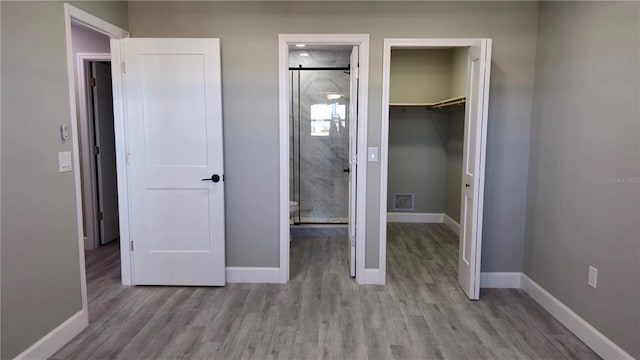 unfurnished bedroom with a closet, light hardwood / wood-style flooring, a spacious closet, and ensuite bath