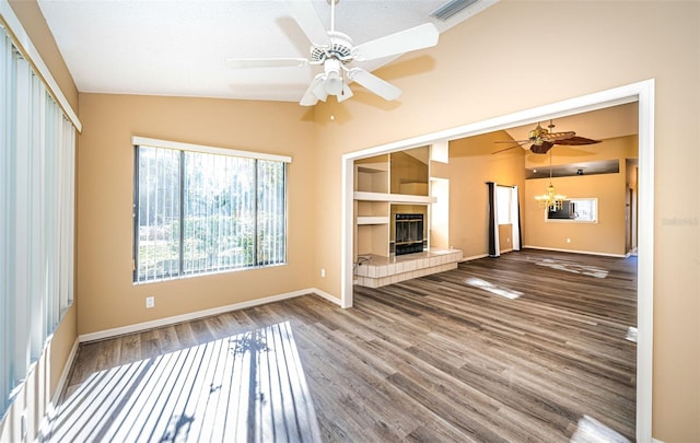 unfurnished living room with a tiled fireplace, vaulted ceiling, ceiling fan with notable chandelier, and hardwood / wood-style floors