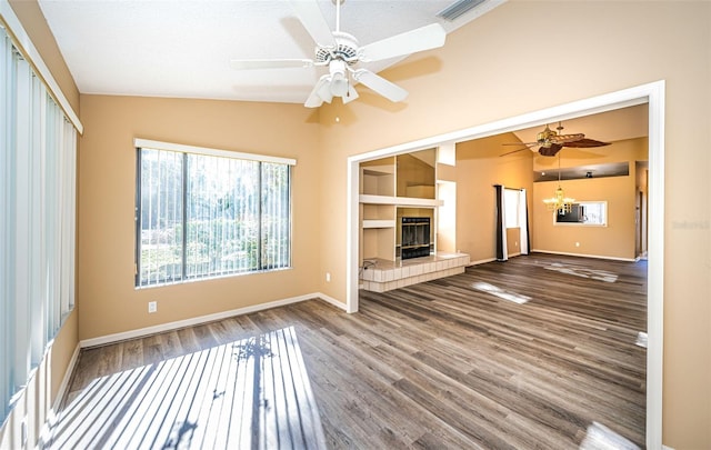 unfurnished living room featuring a tiled fireplace, wood finished floors, ceiling fan with notable chandelier, and vaulted ceiling