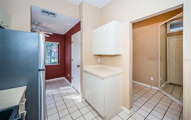 kitchen featuring stainless steel fridge, white cabinets, light tile patterned floors, and ceiling fan