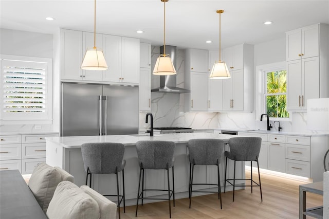 kitchen featuring white cabinets, a kitchen island with sink, high end fridge, light stone counters, and light hardwood / wood-style floors